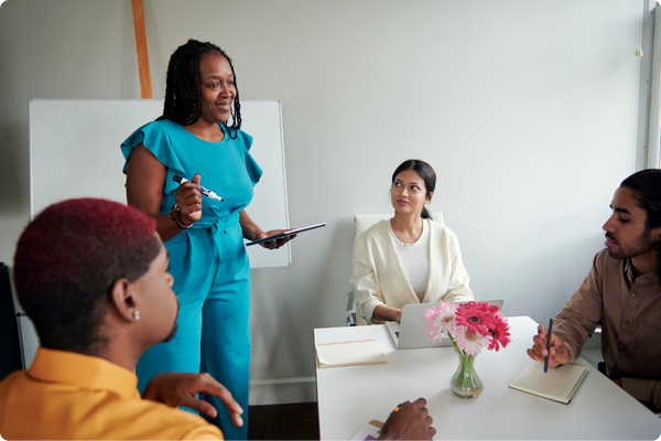 An education leader, holding a tablet, smiling, and meeting with a team in a workroom. An education leader, holding a tablet, smiling, and meeting with a team in a workroom.