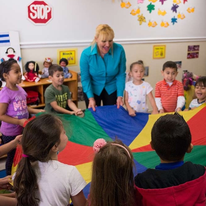 teacher playing parachute with classroom of pre-k children